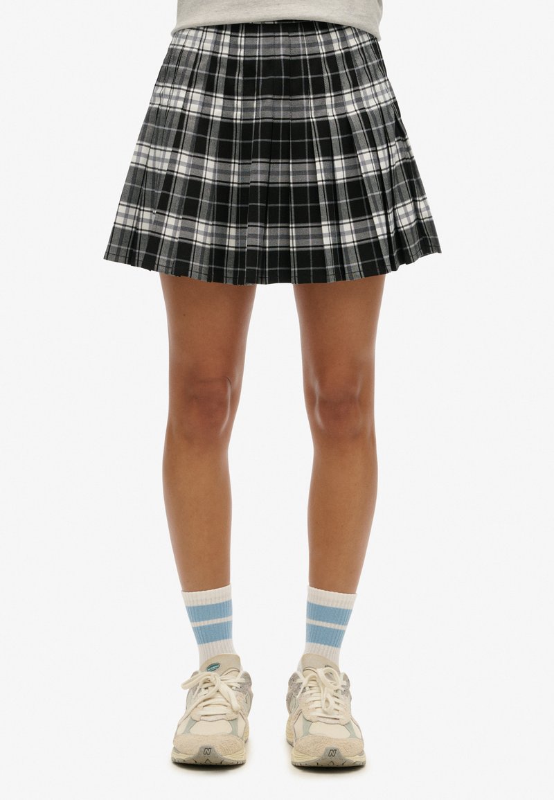 Zwart-witte geplooide geruite rok, tot halverwege het bovenbeen, gecombineerd met lichtgrijze sokken met blauwe strepen en beige sneakers.