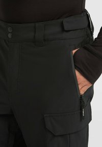 Černé cargo kalhoty s hladkou texturou, které mají dva patentky, kapsu na zip na boku a zesílený design pasu.