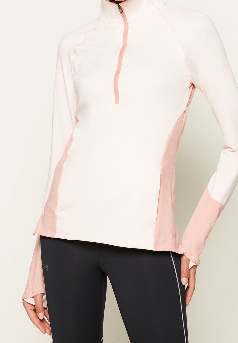 Světle růžová sportovní mikina na zip s růžovými bočními panely, dlouhými rukávy a otvory na palce, vyrobená z elastického materiálu. Spárována s černými legínami.