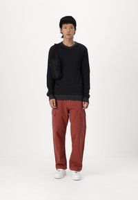 Pulover negru din tricot, pantaloni cargo rustii cu buzunare laterale, adidași albi și o geantă mică de umăr neagră. Design simplu și casual.