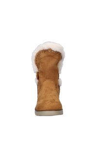 Tan suède enkellaars met een zachte faux fur voering, decoratieve stiksel, en twee pompon-accenten aan de zijkanten. Platte rubberen zool.