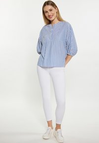 Blusa a righe blu e bianche con maniche a palloncino, scollatura rotonda e sottili pieghe; abbinata a pantaloni bianchi skinny e scarpe da ginnastica casual.