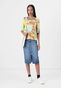 Bunt gemustertes kurzärmliges Hemd in Blau, Orange und Gelb, kombiniert mit einem knielangen Jeansrock und weißen Sneakers.