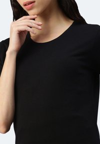 Schwarzes, kurzärmliges Oberteil mit rundem Ausschnitt. Der Stoff wirkt glatt und dehnbar, mit einem figurbetonten Design, das die Silhouette betont.