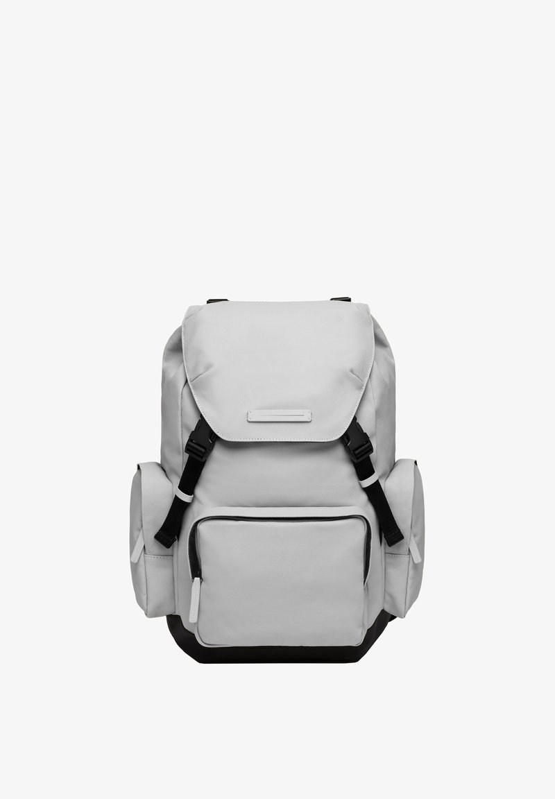 Sac à dos en toile grise avec des bretelles ajustables, un rabat supérieur, plusieurs compartiments et une finition texturée. Accents noirs à la base.