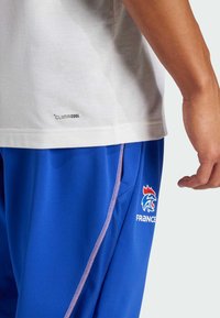 Vit kortärmad skjorta med "CLIMACOOL"-etikett, i kombination med blåa träningsshorts med rosa detaljer och en logotyp av en tupp.