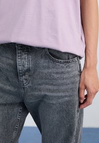 Camiseta de lavanda clara combinada con jeans de mezclilla negros de tiro alto y ajuste tapered. Los jeans tienen bolsillos frontales y una textura ligeramente desgastada.