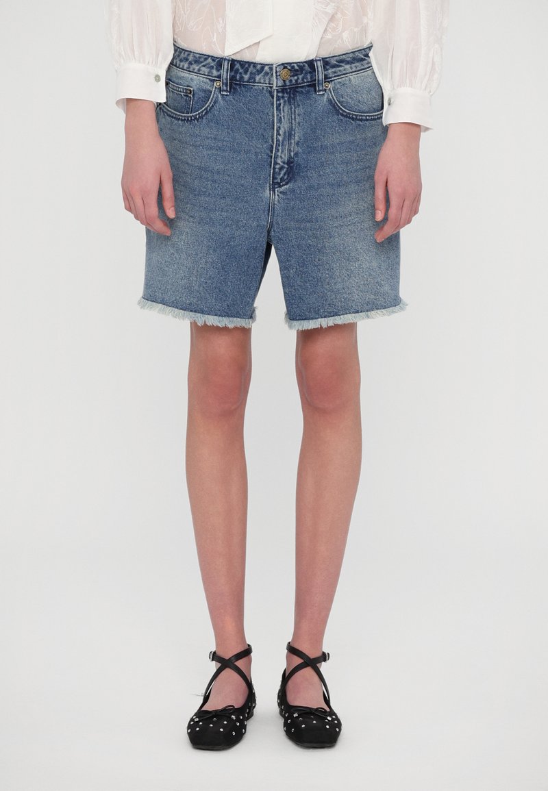 Shorts in denim di colore azzurro chiaro con orlo sfilacciato, abbinati a ballerine nere con pois bianchi e cinturini incrociati.