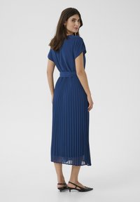 Fodrad blå midiklänning med korta ärmar och smal midja. Slät material med mjuk textur, bärs med svarta slingback-skor.