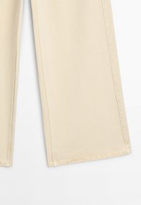 Unterer Teil einer beigen, gerade geschnittenen Hose, zeigt Stoffstruktur und seitliche Nähte vor weißem Hintergrund.