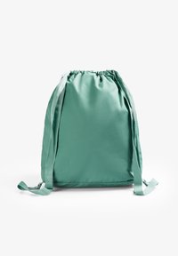 Mochila de tela verde con cordón, de textura suave, con correas ajustables y parte superior fruncida. Diseño simple, de tamaño mediano y construcción ligera.