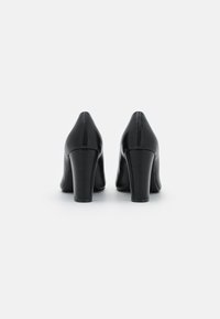 Zapatos de tacón alto de cuero negro con punta afilada y tacón ancho, con una textura suave y costuras limpias a lo largo de las costuras.