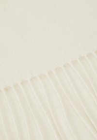 Valge tekk pehmest materjalist, millel on sile tekstuur ja peened äärised, rõhutades selle puhast ja minimalistlikku disaini.