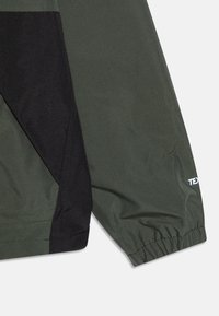 Mörkgrön och svart lättviktsjacka med elastiska mudd, med en slät textur och en logotyp på ärmen.