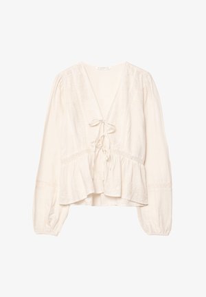 Blouse blanche, légèrement ample, avec des manches longues, un décolleté en V et des détails en dentelle. Présente une fermeture à nouer à l'avant et un ourlet peplum.