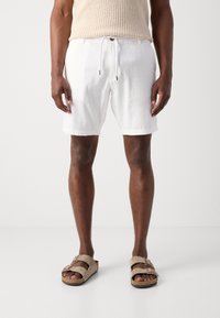 Pantaloni corti bianchi in lino con elastico in vita e cordoncino, abbinati a sandali a scivolo in suede color cammello con due cinturini regolabili.