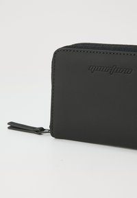 Portefeuille noir avec une texture lisse, fermeture éclair et logo en relief. Dispose d'un tirette de fermeture éclair discrète pour un accès facile. Design compact.