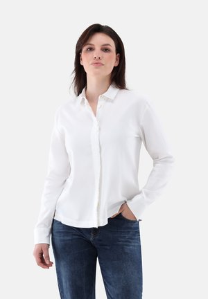 Weißes Hemd mit Kragen, mit Knopfleiste, langen Ärmeln und weichem, glattem Stoff; kombiniert mit dunkelblauen Jeans.