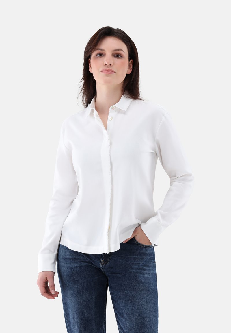 Weißes Hemd mit Kragen, mit Knopfleiste, langen Ärmeln und weichem, glattem Stoff; kombiniert mit dunkelblauen Jeans.