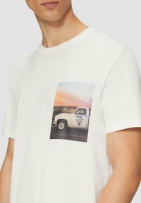 Witte katoen t-shirt met een vierkante afbeelding van een vintage witte vrachtwagen met ondergangskleuren op de achtergrond, tekst op de vrachtwagen zichtbaar.