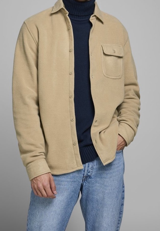 Beżowa flanelowa kurtka z przodu na guziki, z kieszenią na piersi i kołnierzykiem, noszona na granatowym golfie i niebieskich dżinsach.