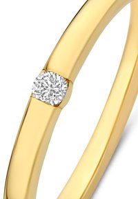 Gold ring with a smooth, rounded band, featuring a small, round diamond embedded at one side. Minimalistic and sleek design.