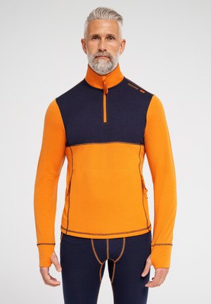 Orange og marineblå pullover med lynlås i halsen, lavet af et glat materiale. Har kontrastsyninger og sidelommer for funktionalitet.
