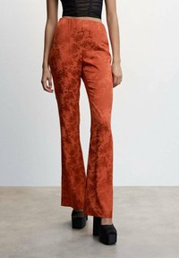 Polvelliset housut poltetun oransseina, joissa on hienovarainen kukkakuosi, valmistettu sileästä kankaasta. Mukana joustava vyötärönauha ja korkeat korolliset platform-kengät.