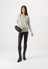 Maglione grigio chiaro a macchie, leggings in pelle nera e stivali neri con tacco. Tiene una borsa a tracolla blu navy con una texture liscia.