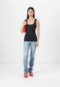 Schwarzes Tanktop, hellblaue Jeans und rote Absätze. Das Top ist figurbetont mit einem runden Halsauschnitt. Die Tasche ist eine kleine, rote Schultertasche.