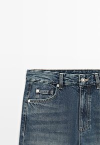 Niebieskie dżinsy z denimu z przednimi kieszeniami, srebrnymi nitami, szlufkami na pasek i metalowym zapięciem na guzik na białym tle.