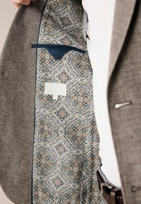 Grau Hahnentwist-Blazer mit einem dekorativen Futter in blau-beigem Muster, ausgestattet mit einer Tasche und einer glatten Textur.