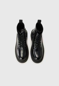 Bottes noires en cuir à lacets avec fermetures éclair latérales, présentées de dessus sur un fond blanc.