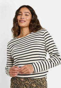 Top de manga larga en color crema con rayas horizontales negras, con un escote barco y costuras visibles, combinado con pantalones de estampado de leopardo.