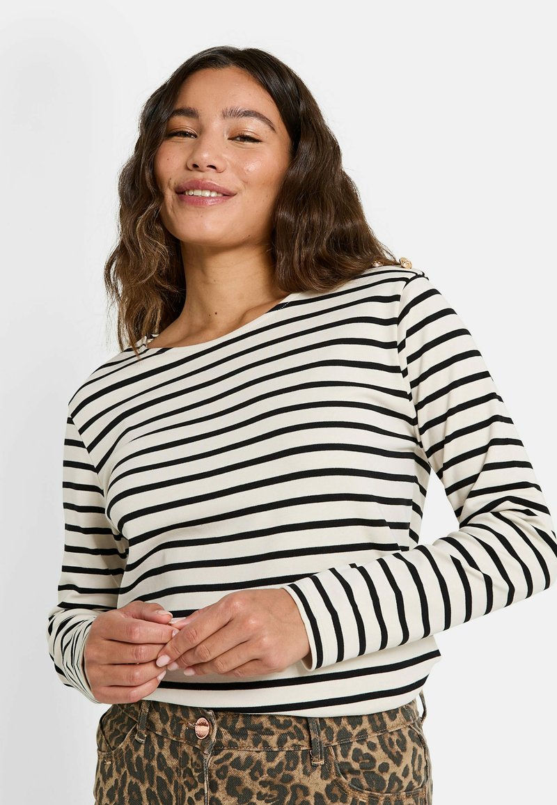 Top de manga larga en color crema con rayas horizontales negras, con un escote barco y costuras visibles, combinado con pantalones de estampado de leopardo.