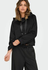 Juodas trumpas džemperis su raišteliu, laisva forma ir guminiais rankogaliais. Derinamas su derančiais juodais džinsais, sudarant komfortišką aprangą.