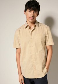 Camisa de botones de manga corta en amarillo con un patrón geométrico de diamantes. La tela tiene una textura suave y un ajuste regular, con un cuello clásico.