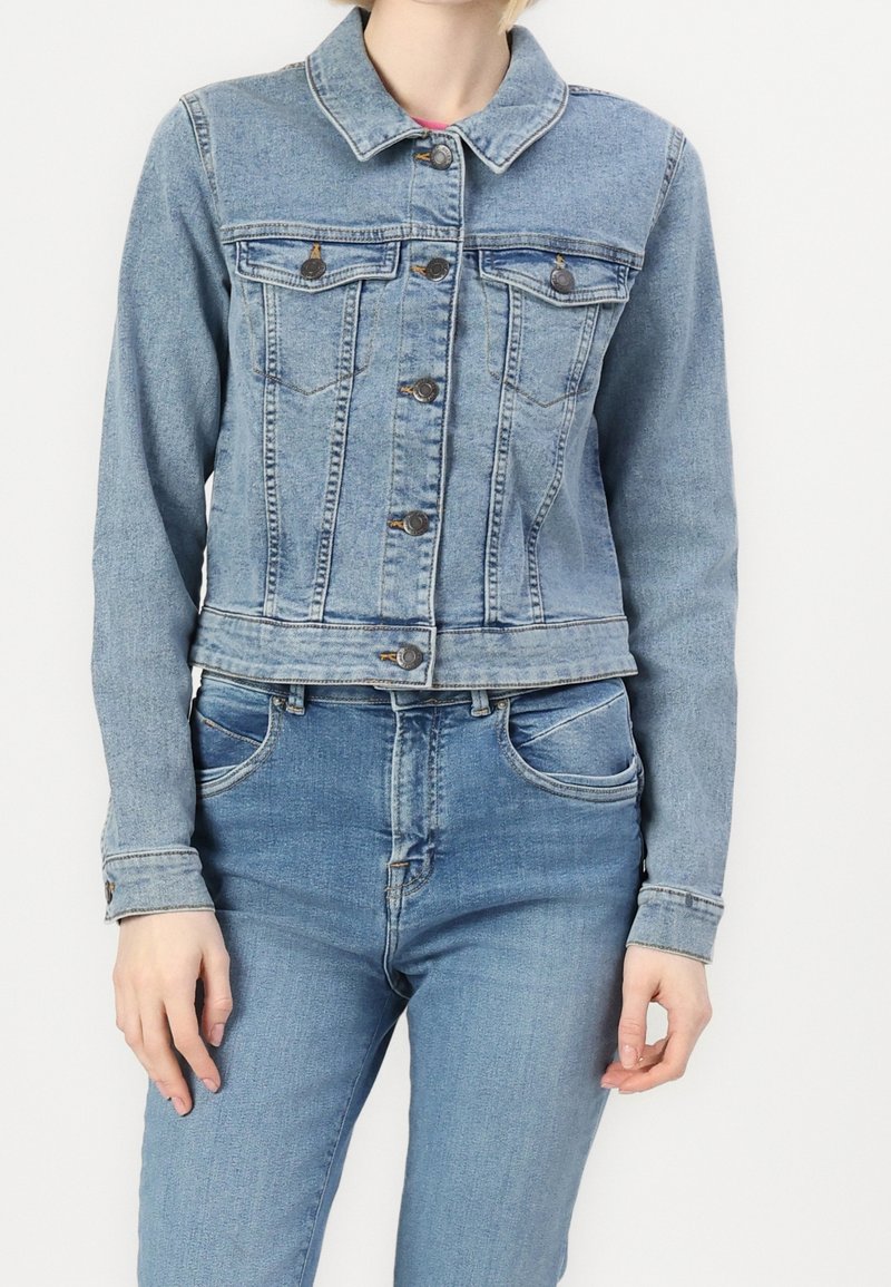Jasnoniebieska kurtka dżinsowa, z kołnierzykiem, przednimi kieszeniami i zapięciem na guziki. Materiał ma klasyczną, tkana fakturę.