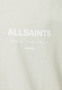 Šviesiai žalia medvilninė marškinėliai su balta ekranuotu tekstu: „ALLSAINTS“ ir „LONDON“ bei papildomais simboliais. Lygus paviršius, kasdieniškas dizainas.