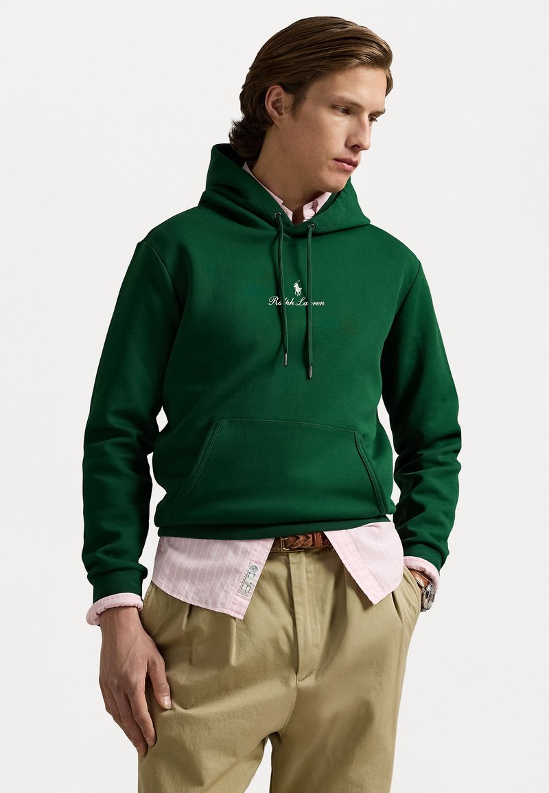 Green cotton hoodie with drawstrings and front pocket, featuring white "Ralph Lauren" logo. Layered over a light pink button-up shirt.