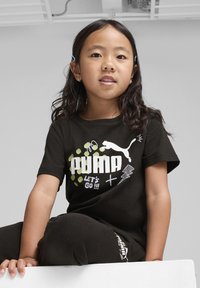 Čierne bavlnené tričko s bielym a zeleným grafickým textom "PUMA LET'S GO !!!" a logom mačky. Skombinované s čiernymi nohavicami, nosené dieťaťom.