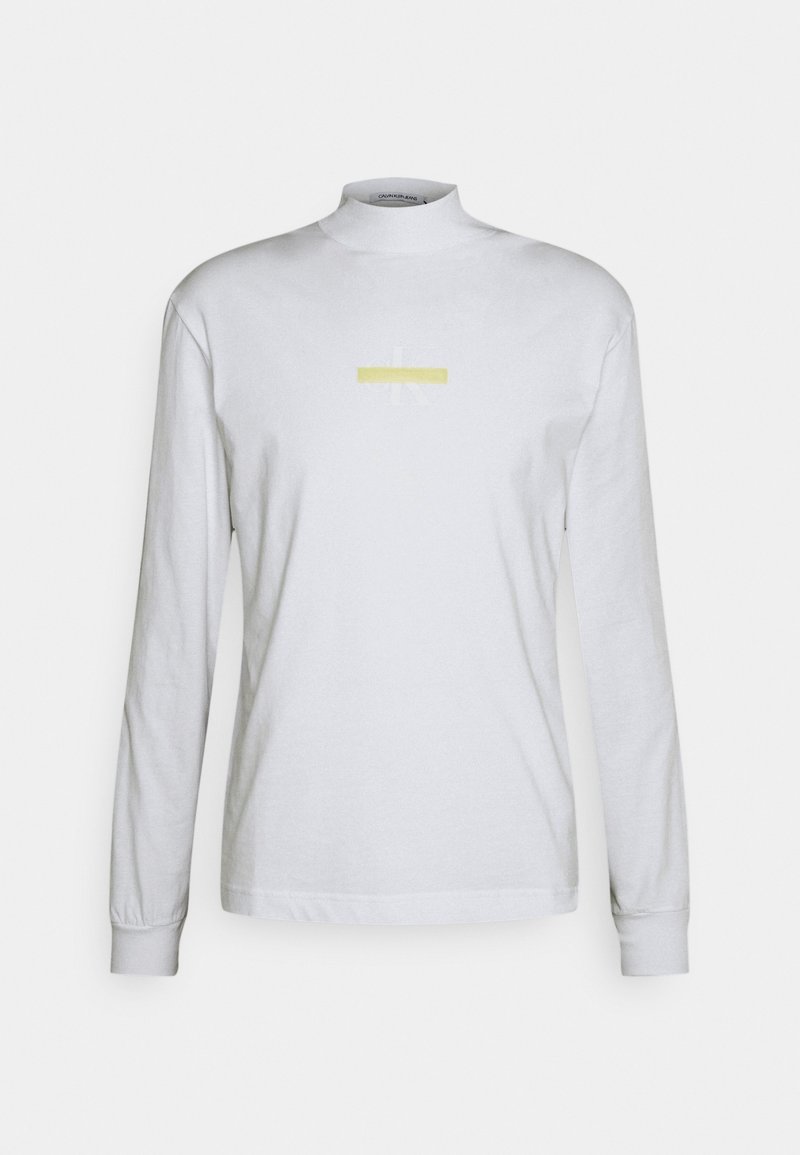 Bílé tričko s dlouhým rukávem a vysokým výstřihem. Na středu je jemný žlutý grafický motiv a světle šedý design. Měkká bavlněná tkanina.