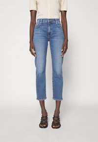 Modré džínové kalhoty s vysokým pasem, rovného střihu a zkrácené délky s třepícím se lemem. V kombinaci s černými sandály nařasenými na noze.