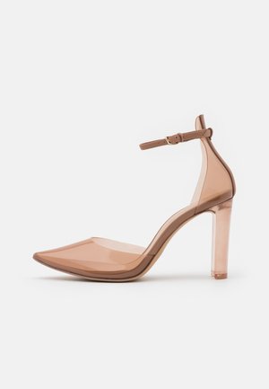 Chaussure à talon aigu en plastique transparent de couleur nude, avec un bout pointu, une bride autour de la cheville et un talon bloc transparent. Texture lisse et design minimaliste.