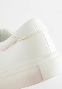 Baskets blanches en simili cuir lisse. Présentent un logo subtil en relief, des coutures ton sur ton et une semelle épaisse et robuste.