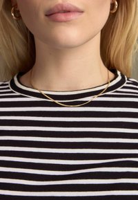 Gestreiftes schwarz-weißes Baumwollshirt mit rundem Halsausschnitt, kombiniert mit einer dünnen goldenen Kettenhalskette, die auf dem Schlüsselbein liegt.