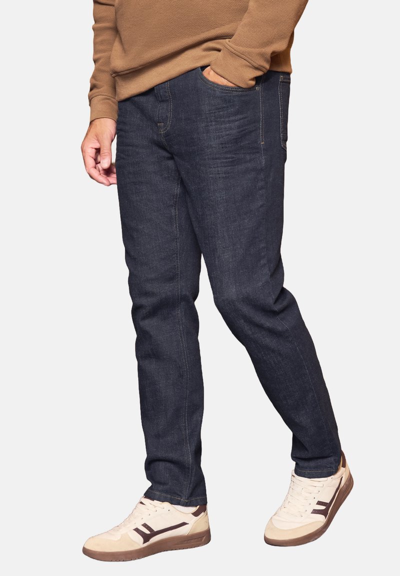 Vaqueros de denim azul oscuro con corte recto, presentando costuras sutiles y bolsillos laterales, combinados con zapatillas de deporte de color blanco sucio.