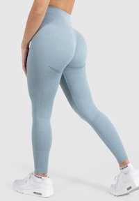 Legginsy z wysokim stanem w kolorze jasnoniebieskim, o prążkowanej strukturze, z gładką teksturą i subtelnymi detalami konturowymi z tyłu, w połączeniu z białymi trampkami.