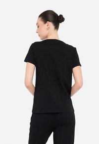 Camiseta negra de manga corta hecha de una tela suave, con un cuello redondo clásico y un ajuste relajado. Diseño simple sin patrones ni acentos.