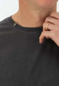 Maglietta grigia scura a maniche corte con scollatura rotonda, caratterizzata da un accento sottile di cuciture gialle, bianche e nere sul colletto.